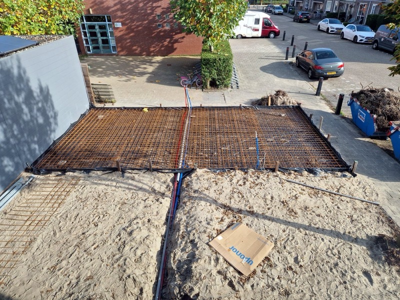 Betonwapening met leidingen voor water en elektra op de bouwplek van een tuinkamer