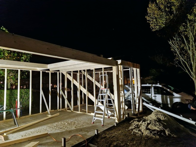Houtskelet van een tuinkamer in aanbouw, verlicht in de avond
