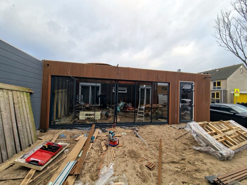 Tuinkamer in aanbouw met houten gevel en net geplaatste glazen schuifwanden