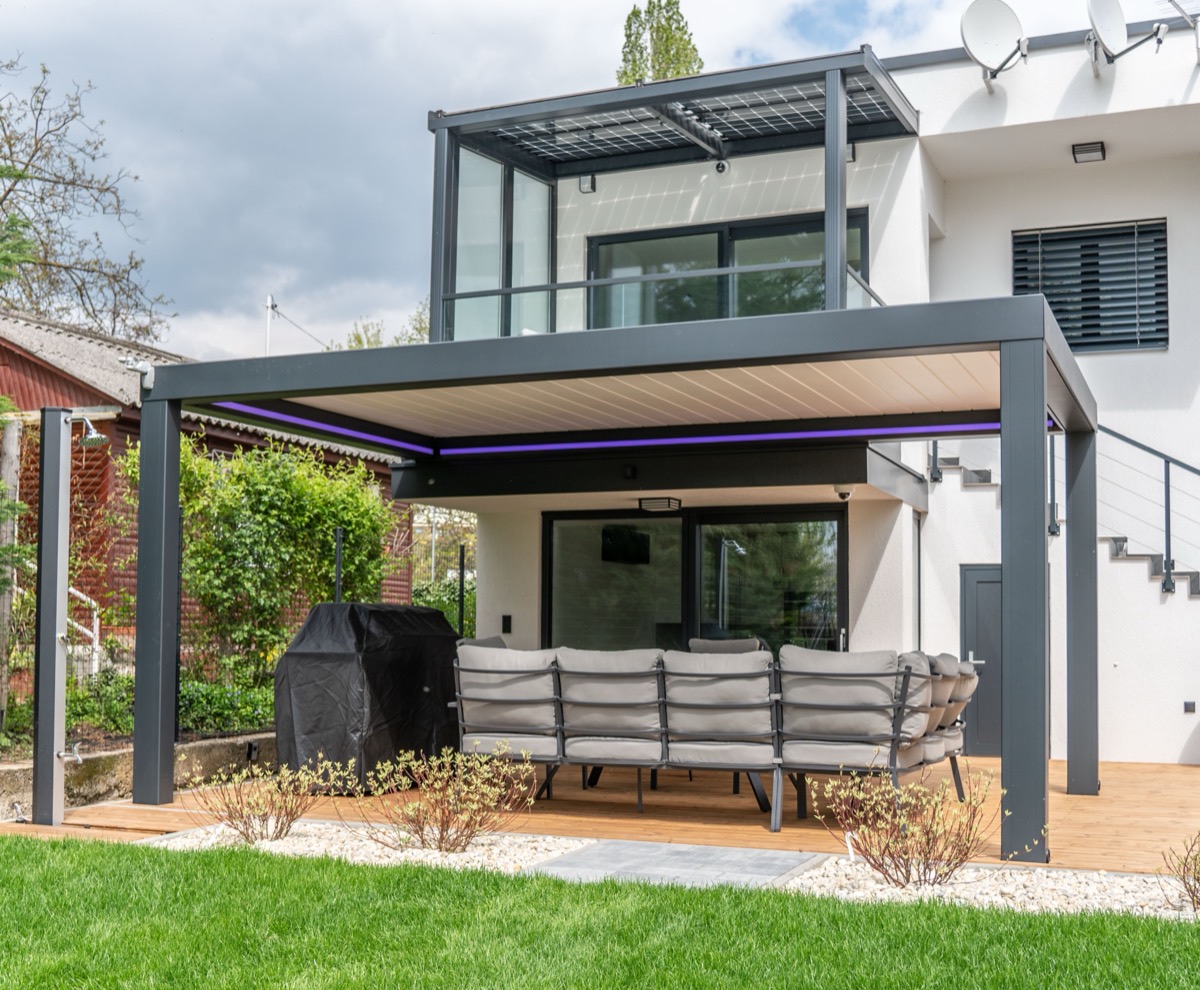Lamellendak in zwart aluminium aan een moderne woning, lamellen open boven een loungeset