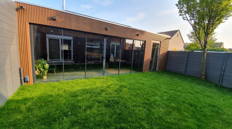 Tuinkamer met verticale houten gevelbekleding en een lange glazen schuifwand, gezien vanaf het gazon