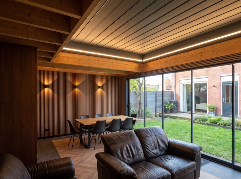 Tuinkamer met eettafel, houten plafond met LED-lichtlijn en glazen schuifwand naar de tuin