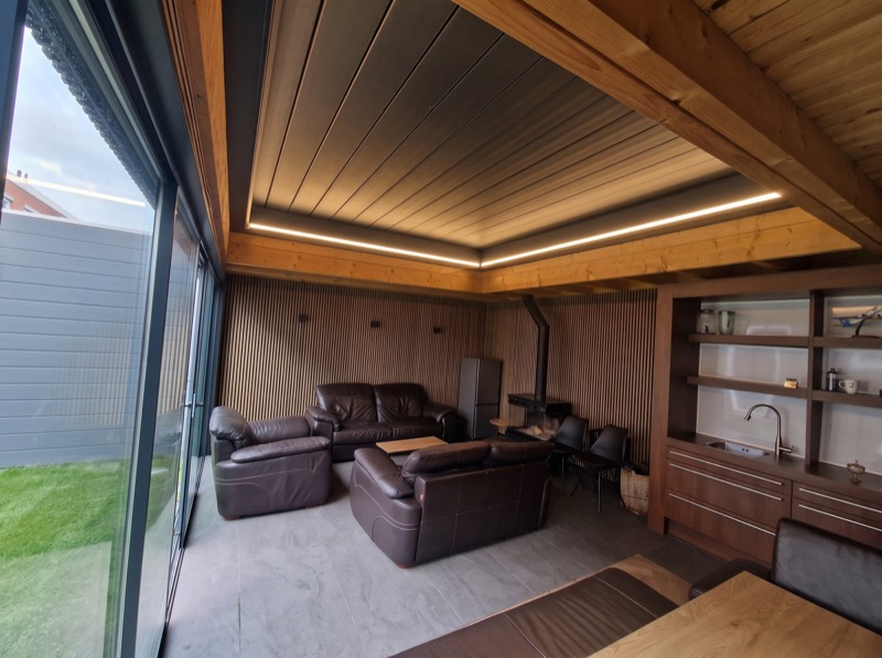 Loungehoek in een tuinkamer met leren banken, houtkachel en glazen wand naar de tuin