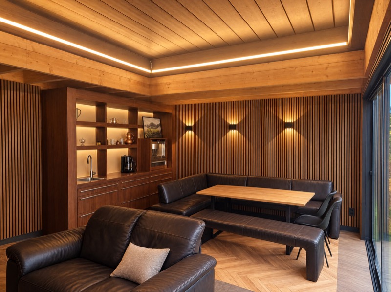 Interieur van een tuinkamer met houten lamellenwanden, wandlampen, een LED-lichtlijn in het plafond en een inbouwkast met spoelbak