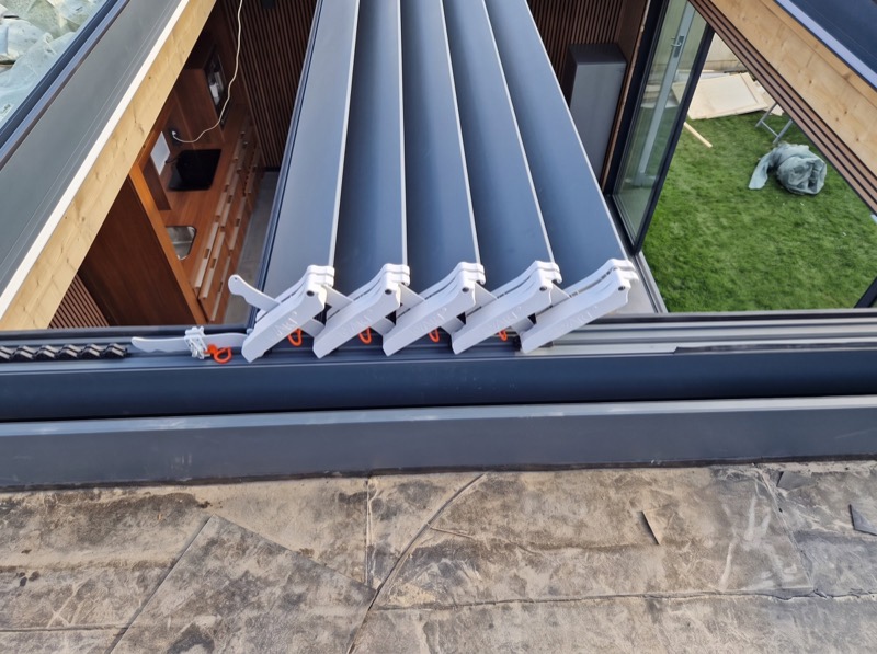 Antraciet aluminium lamellen van een lamellendak, half opengedraaid in de dakopening van een tuinkamer